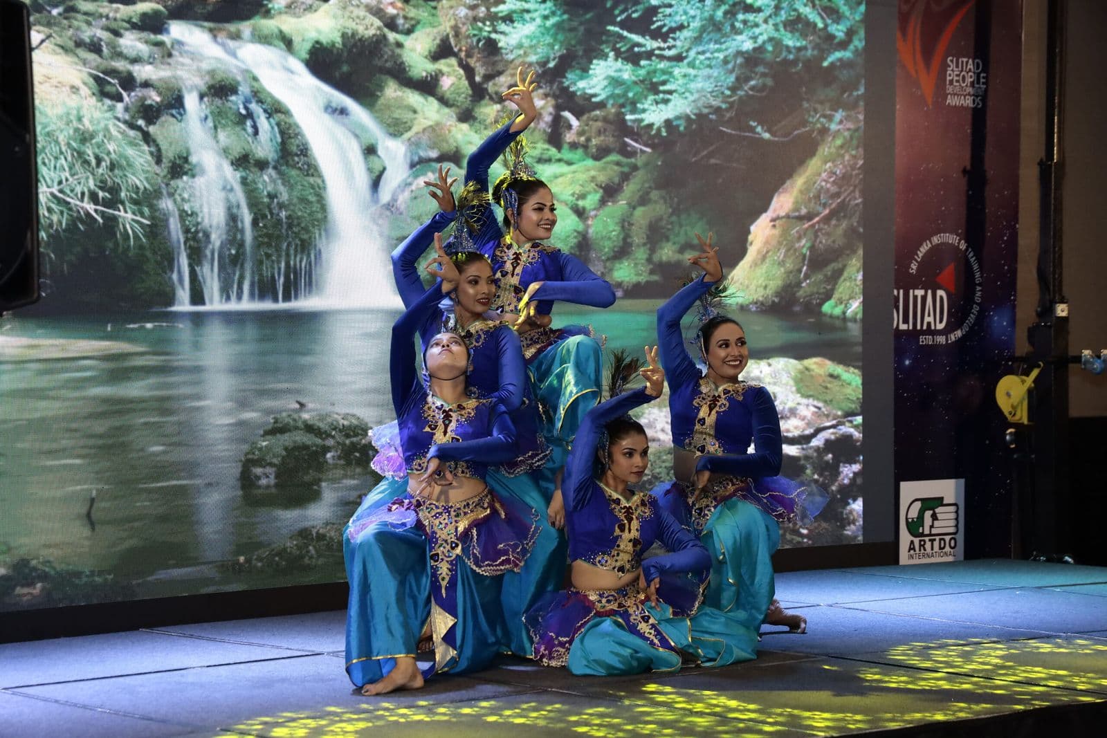 Traditional dancers before a waterfall backdrop at the People Development Awards
