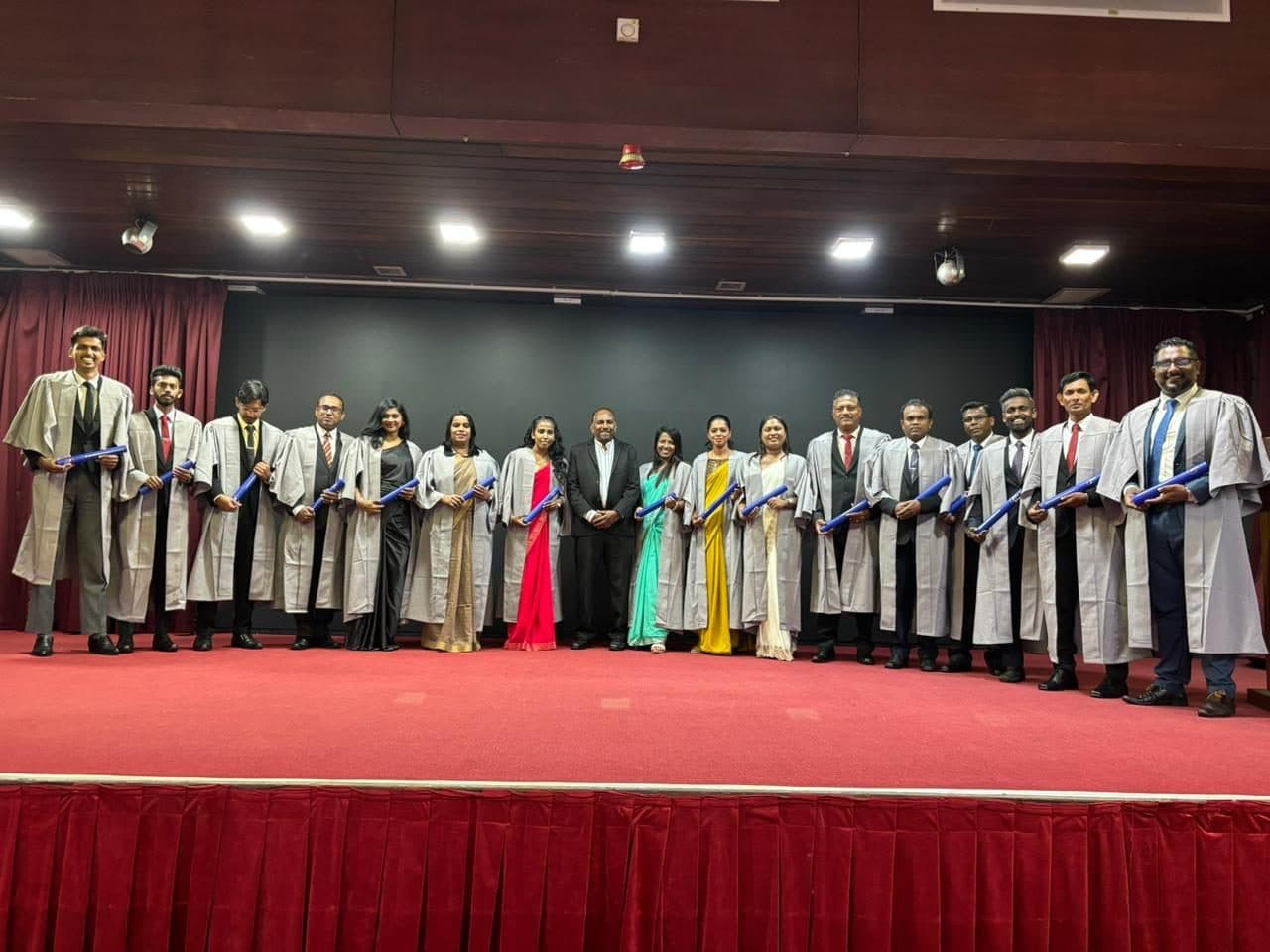 SLITAD graduates in gowns with their diplomas on stage